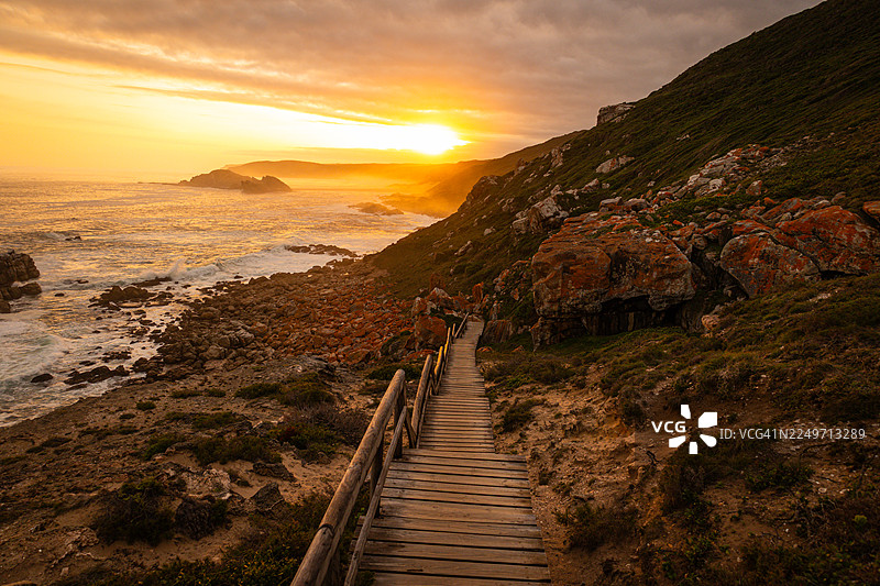 南非罗伯格自然保护区的风景优美的海岸步道，在黄金时刻拍摄，展现了岩石悬崖、木制栈道和海景。图片素材