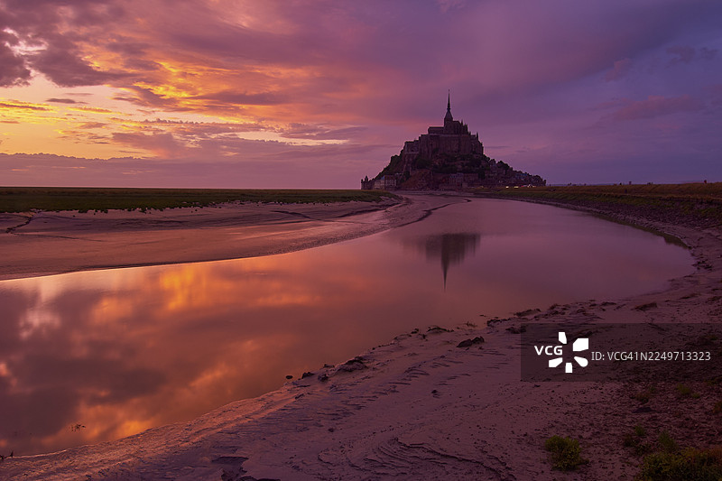 夏季日落时分的圣米歇尔山，天空戏剧性地变幻，水面倒映着山景，地点位于法国诺曼底布列塔尼的圣米歇尔山。图片素材