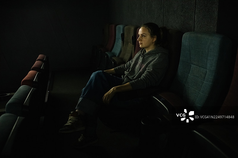 一个孤独的身影坐在昏暗的电影院里，在空无一人的座位排中静静地反思。图片素材