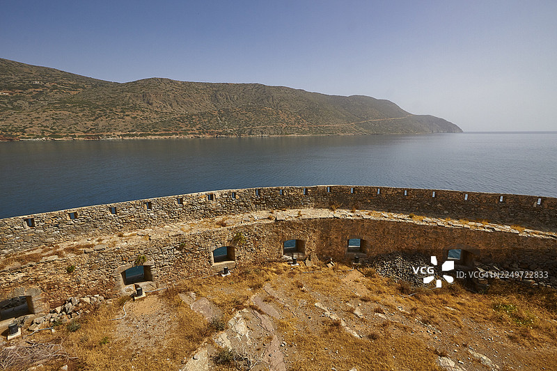俯瞰平静大海的古老石墙，背景是群山，天空湛蓝，威尼斯海堡，麻风病岛，斯皮纳隆加，埃卢达湾，米拉贝罗湾，东克里特，克里特，希腊岛屿，希腊图片素材