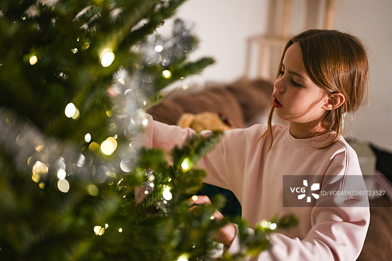 小女孩正在装饰温馨的圣诞树彩灯图片素材