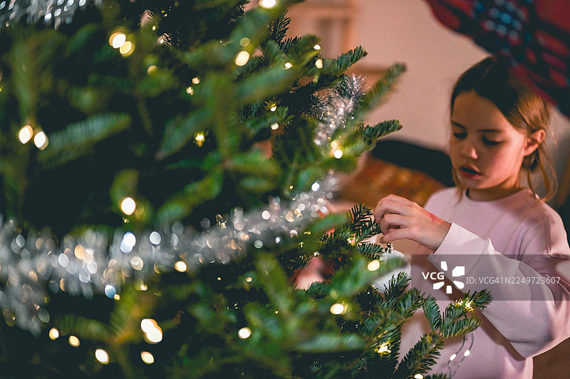 女孩用灯和彩带装饰圣诞树图片素材