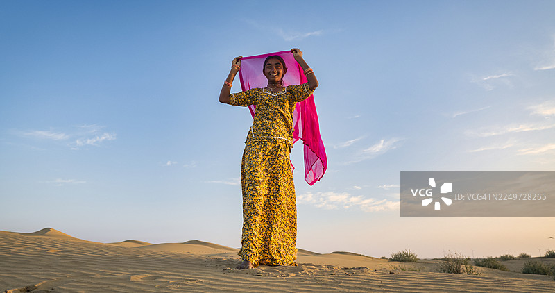 快乐的印度女孩在沙丘上跳舞，背景是沙漠村庄，印度图片素材