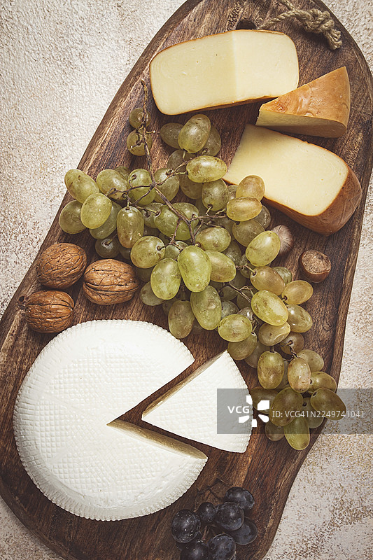 格鲁吉亚奶酪，包括伊梅列季和烟熏苏鲁古尼，以及葡萄和坚果，摆放在砧板上，展现格鲁吉亚美食，无人物出镜。图片素材