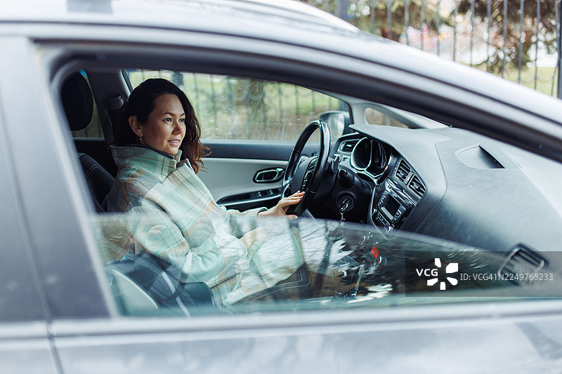 一位穿着格子外套的女士在白天通勤时，在车内放松而自信地驾驶图片素材