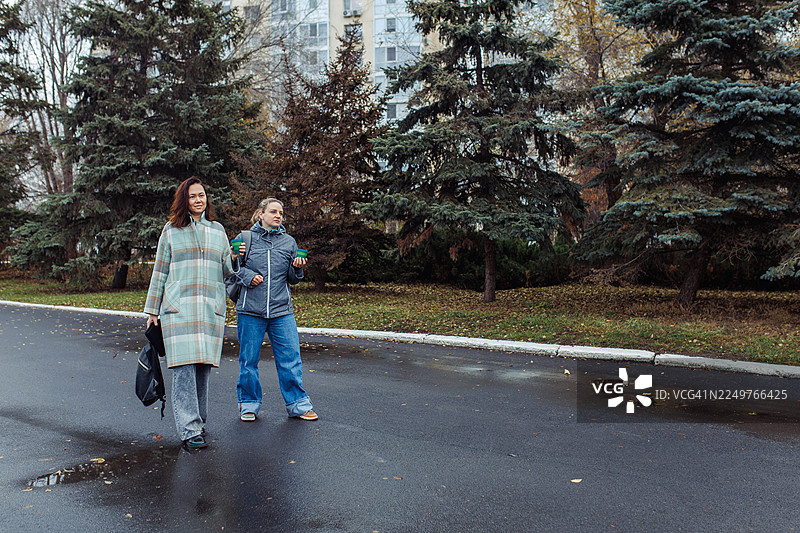 秋日雨天，两位朋友在公园里一边散步一边拿着咖啡杯图片素材
