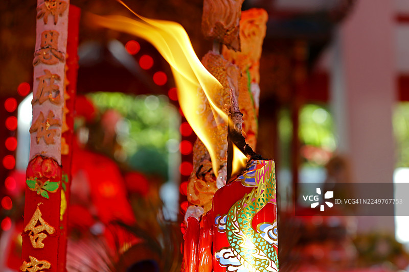 带有金色龙纹的红色装饰蜡烛，火焰细长，旁边摆放着带有中国字样的华丽红色熏香棒或香柱。图片素材