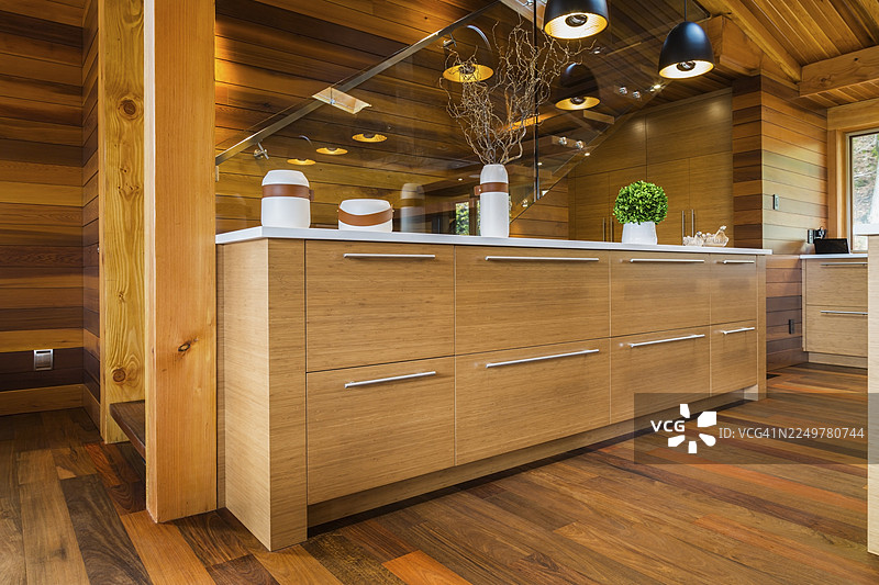 加拿大魁北克一栋豪华住宅，房屋采用染色雪松和木材建造，室内铺设伊佩木地板，厨房内设有带玻璃栏杆的楼梯，旁边是竹木餐边柜，配有白色石英台面，上方悬挂着黑色工业风格的吊灯。图片素材