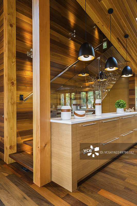加拿大魁北克一栋豪华的染色雪松和木材房屋内，厨房配有IPE木地板，竹木餐边柜配有白色石英台面，黑色工业风格吊灯照明，旁边是带透明玻璃栏杆的楼梯。图片素材