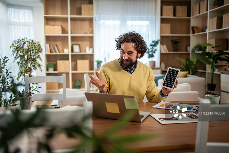 居家办公的男子在视频通话中展示太阳能电池板图片素材