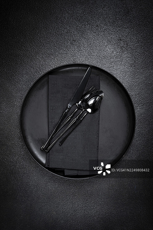 食物背景，带有空的黑色盘子、黑色餐具和餐巾，置于黑色背景上，餐桌布置，俯视视角，无人图片素材
