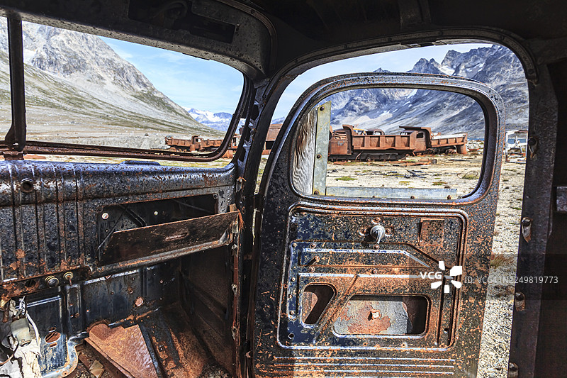 锈迹斑斑的汽车内部视角，背景是陡峭的山脉，这是第二次世界大战时期美国空军基地遗址，位于格陵兰东部的伊卡特克峡湾。图片素材