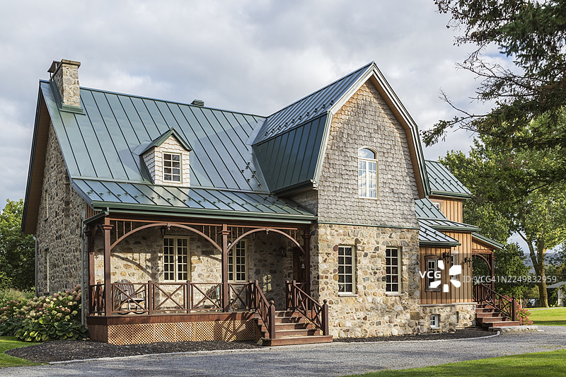 加拿大1826年老式乡村风格的田野石砌房屋外观，带有垂直木板壁板、雪松瓦和绿色的直立缝金属屋顶，摄于夏末，加拿大魁北克省图片素材