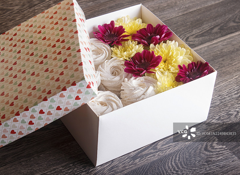 白色的盒子，里面装着自制的白色风神花、向日葵和菊花，背景是灰色的木板。图片素材