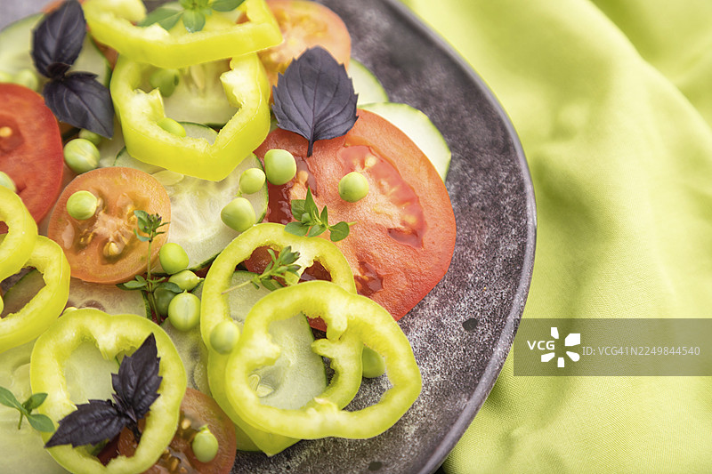 绿色豌豆、番茄、辣椒和罗勒制成的素食沙拉，放在绿色纺织品上。俯视，特写，选择性聚焦图片素材