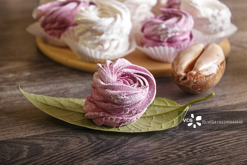 粉白相间的自制棉花糖（zephyr）放在圆木板上，木板上散落着海螺，背景为灰色木纹图片素材