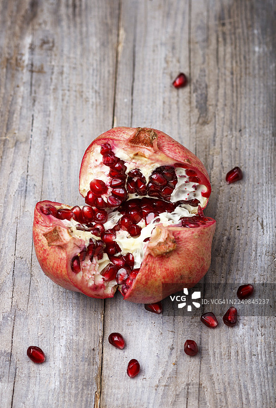 一个打开的成熟石榴，籽呈石榴石色，背景为乡村木质图片素材