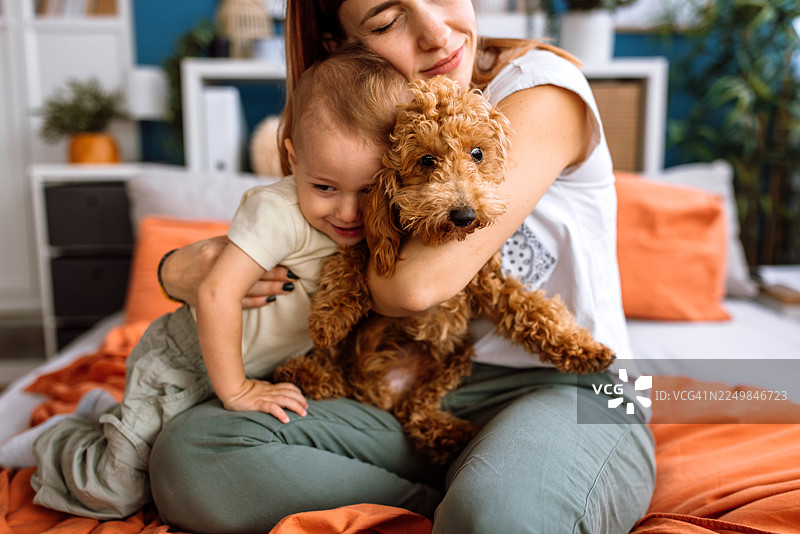 一位母亲拥抱她的小男孩和可爱的狗狗。图片素材