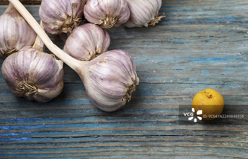 蓝色质朴木质背景上新鲜的紫皮蒜和黄色的水果。对比的概念图片素材