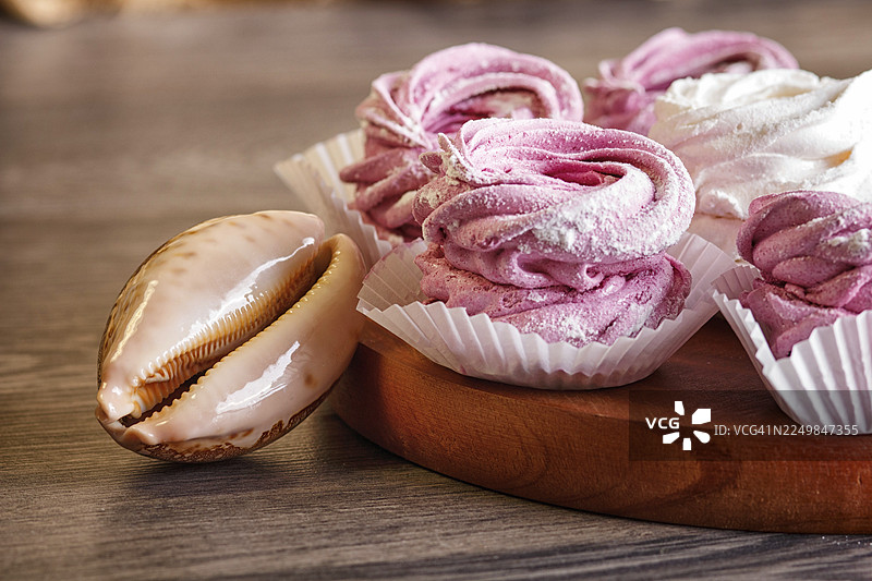 粉白色手工棉花糖（zephyr）放在圆形木板上，木板上散落着贝壳，背景为灰色木质图片素材