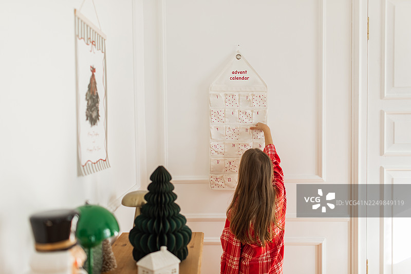 孩子在白色墙壁前伸手去拿圣诞倒数日历，营造温馨的圣诞氛围图片素材