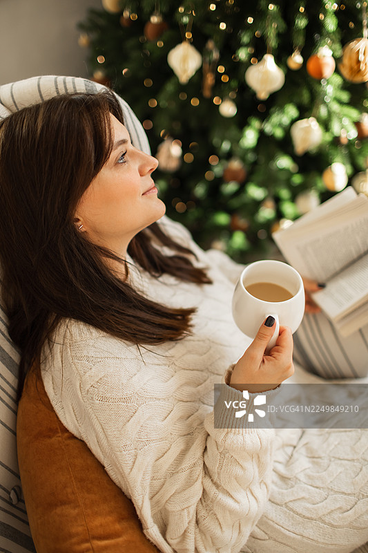 温馨家居中，女子在圣诞树旁惬意地享用咖啡，放松身心。图片素材