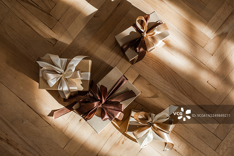 铺设在木地板上的精美礼品盒，系着优雅的丝带，沐浴在温暖的光线下图片素材