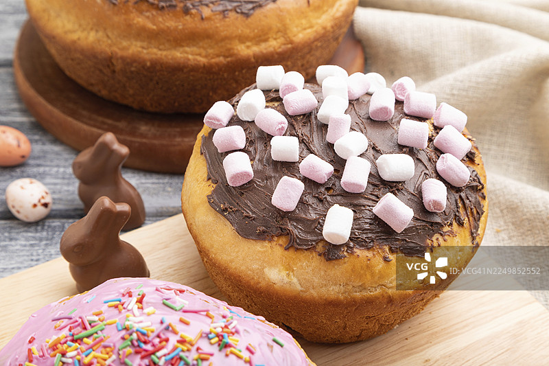 灰色木质背景搭配亚麻织物的自制釉面复活节馅饼，上面装饰着巧克力彩蛋和兔子。侧视图，特写图片素材