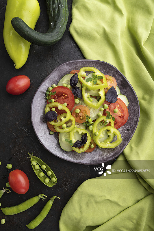 绿色豌豆、番茄、辣椒和罗勒制成的素食沙拉，黑色混凝土背景和绿色纺织品。俯视，特写，平面布置图片素材