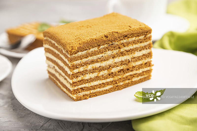 自制蜂蜜蛋糕，搭配牛奶奶油和薄荷，旁边放着一杯咖啡，背景为灰色混凝土和绿色纺织品。侧视图，特写，选择性对焦图片素材