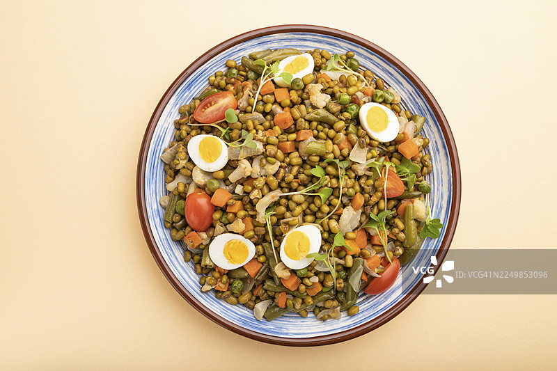 粉橙色背景上的绿豆粥，配有鹌鹑蛋、番茄和微型蔬菜苗。俯视，特写。图片素材