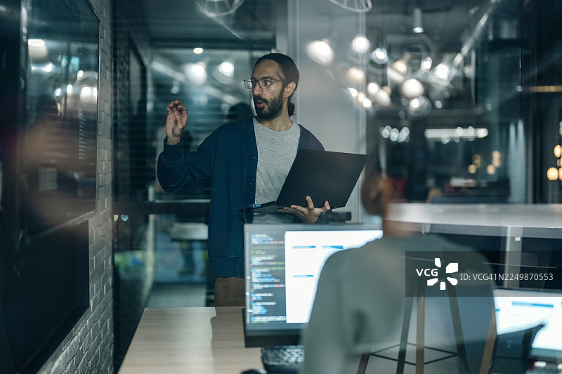 软件工程师们在办公室协作项目，讨论客户需求概念，绘制工作流程图，并在电脑显示器上分析代码。图片素材