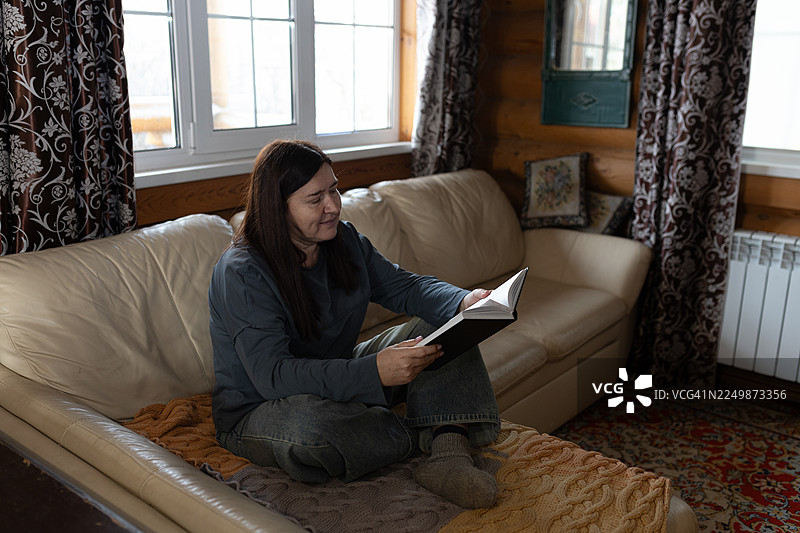 温馨的木屋客厅里，一位女士舒适地坐在米色沙发上阅读图片素材