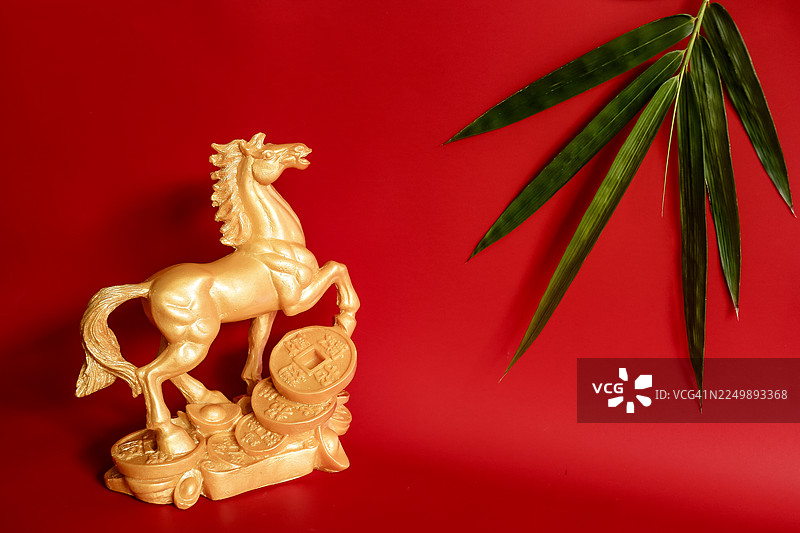 金色石头马雕塑和竹叶在红色背景上图片素材