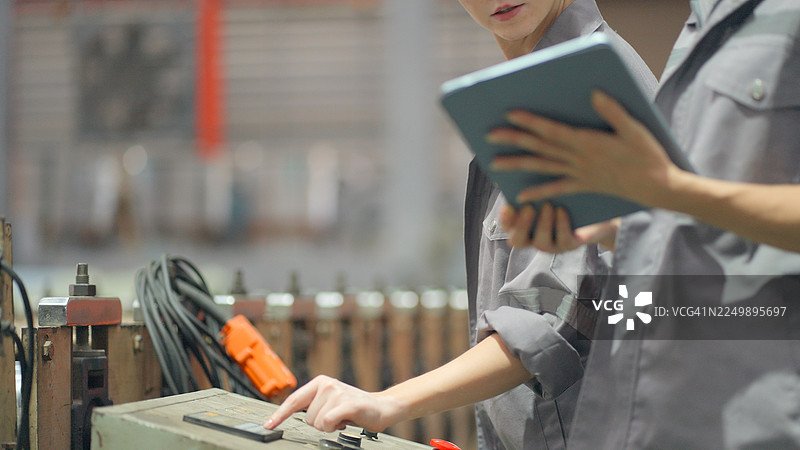 特写。工程师、技术员或运营经理身穿防护服，正在审查生产控制系统，并走向金属零件制造厂仓库，检查用于生产的原材料运输系统。图片素材