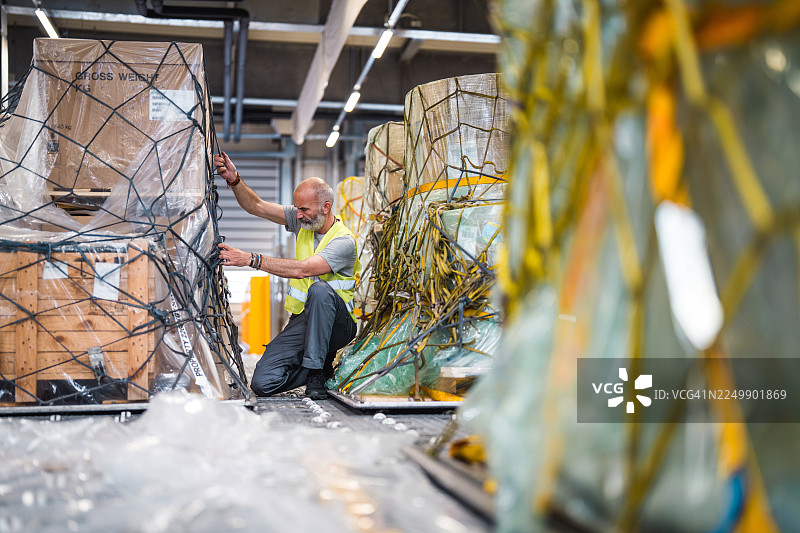 明亮机场仓库内，成熟男性工人正在固定货物图片素材