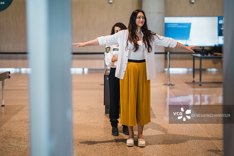 年轻的西班牙裔女性机场安检人员，双手伸展，正在扫描乘客。图片素材