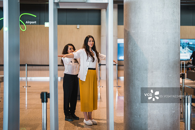 年轻的西班牙裔女性机场安检人员在光线明亮的机场环境中为女性旅客进行扫描图片素材