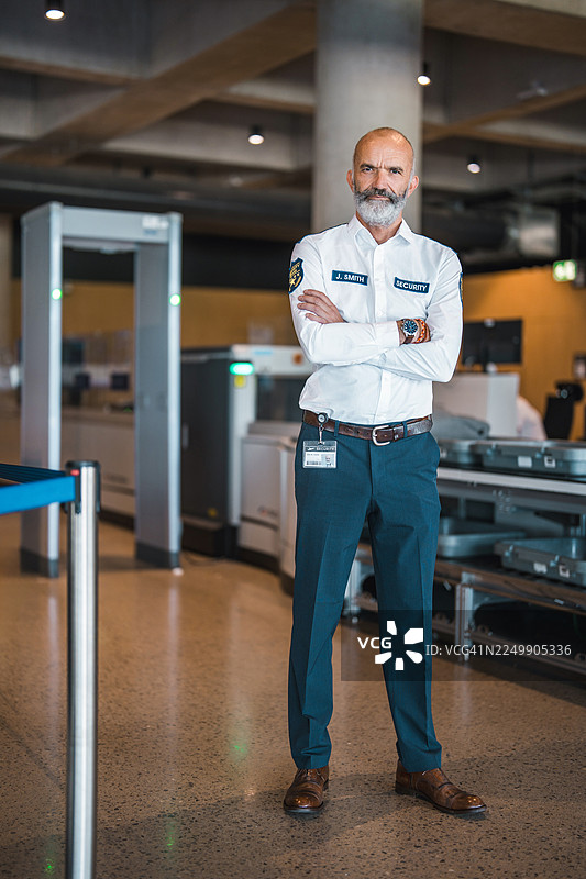 自信的成熟男性机场安检人员，双臂交叉站立在现代航站楼内图片素材