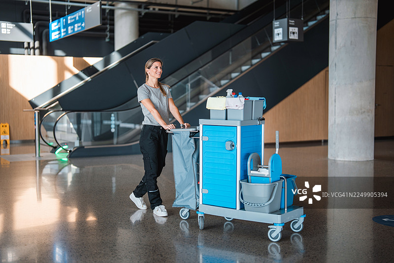 中年白人女性机场清洁工，推着清洁车在航站楼内图片素材