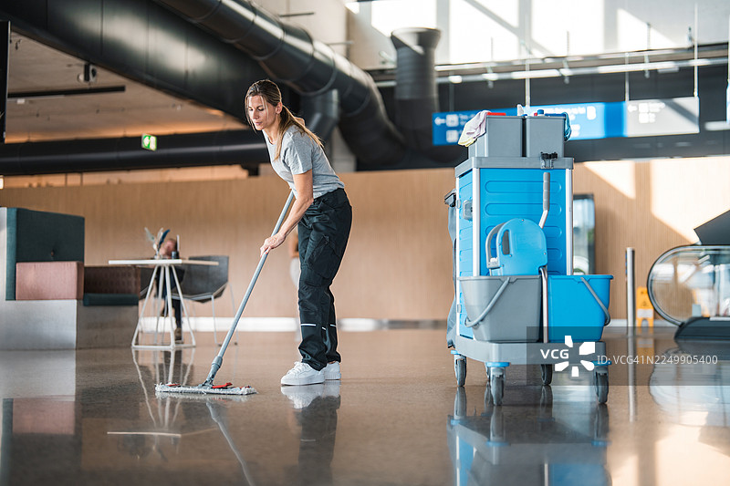 中年白人女性机场清洁工正在拖拭光亮如镜的候机楼地板图片素材