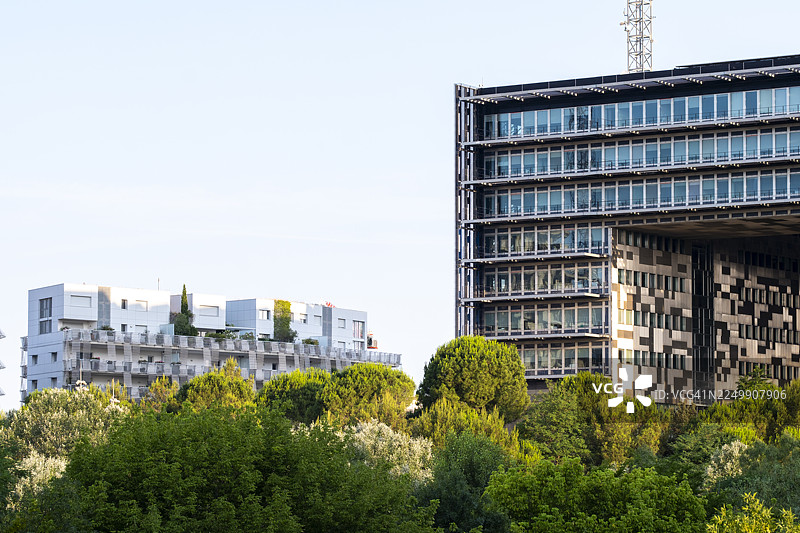 蒙彼利埃市政厅与邻近的现代建筑以及广阔的树冠的广阔视野，勾勒出不断发展的城市景观图片素材