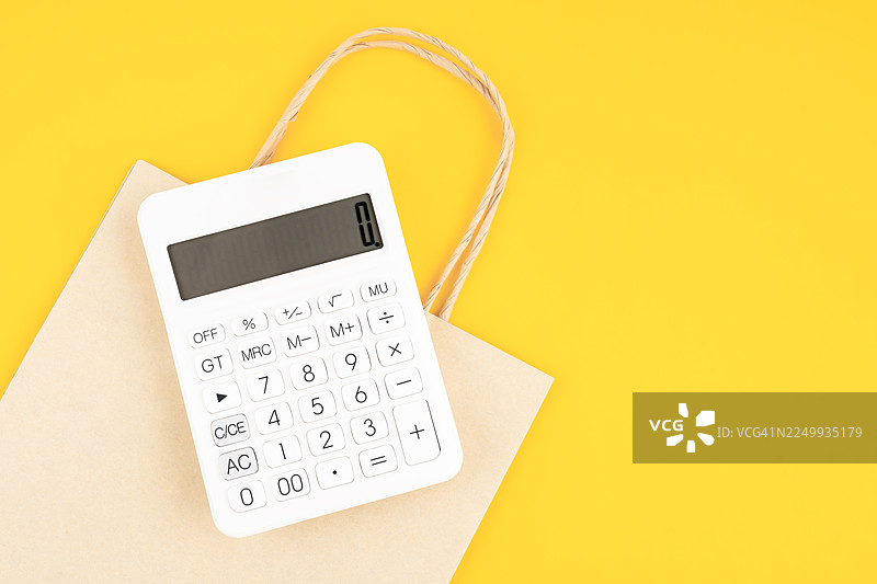 白色计算器放在黄色背景上的小型纸质购物袋中，俯视角度。图片素材