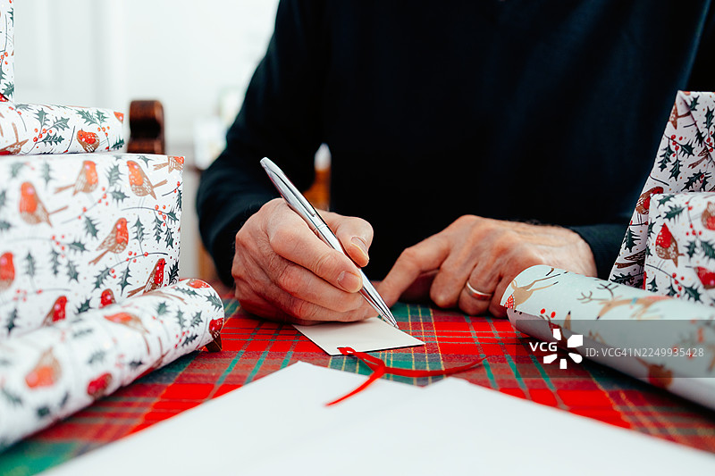 老人的手在家中写圣诞礼物标签，周围摆满了包装好的礼物图片素材