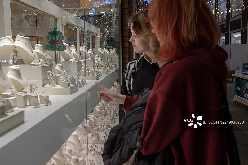 两位女士在假日商店的玻璃橱窗里欣赏珠宝图片素材