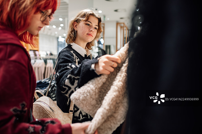 两位好友在服装店一起购物，正在查看一件柔软的人造皮草外套图片素材