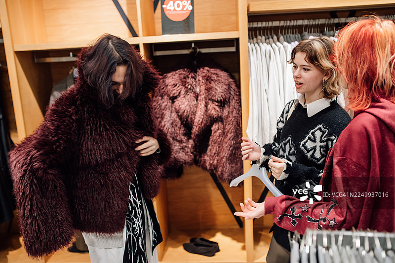 朋友们逛街买时尚：一群年轻女性在店里试穿舒适的毛绒外套图片素材