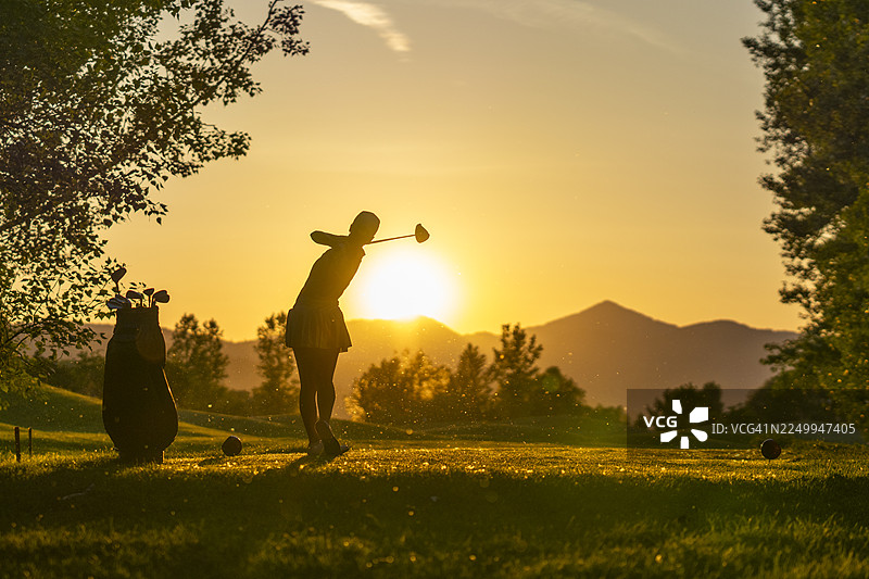 年轻高加索女性高尔夫球手在日落时在发球台挥动发球杆，神情坚毅图片素材