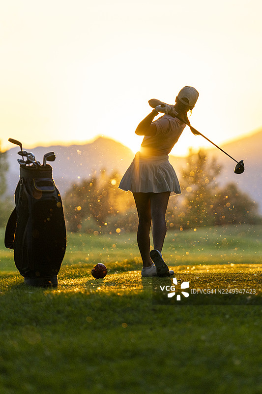 日落时分，高尔夫球场上一位年轻的高加索女性高尔夫球手正在挥动发球杆图片素材