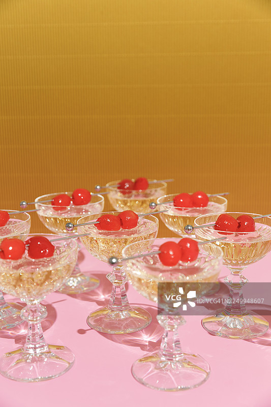 金色粉色背景上重复的水晶玻璃杯，里面盛有香槟和鸡尾酒樱桃图片素材